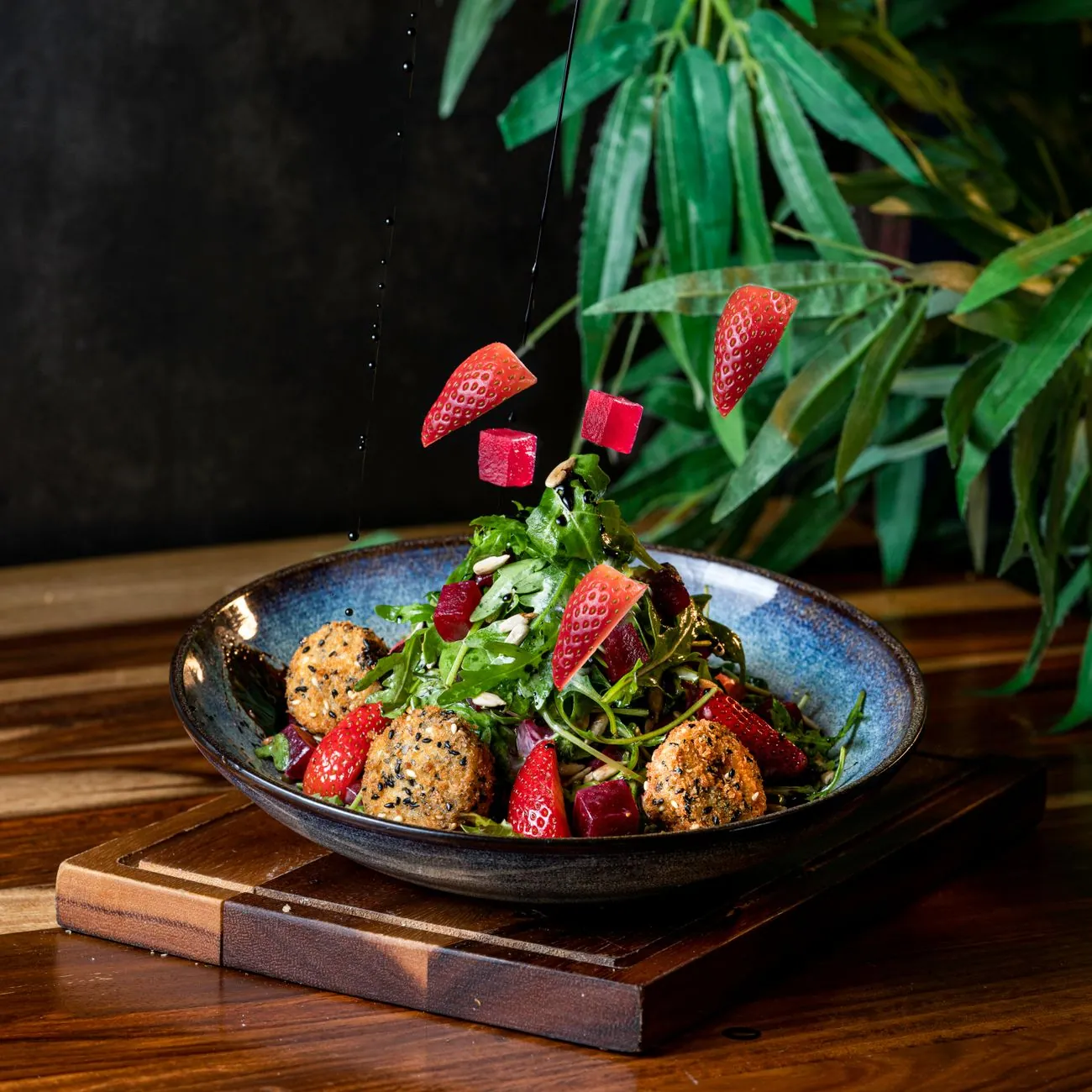 Đĩa salad rau mầm với dâu tây và củ dền bên chậu cây xanh trên nền tối